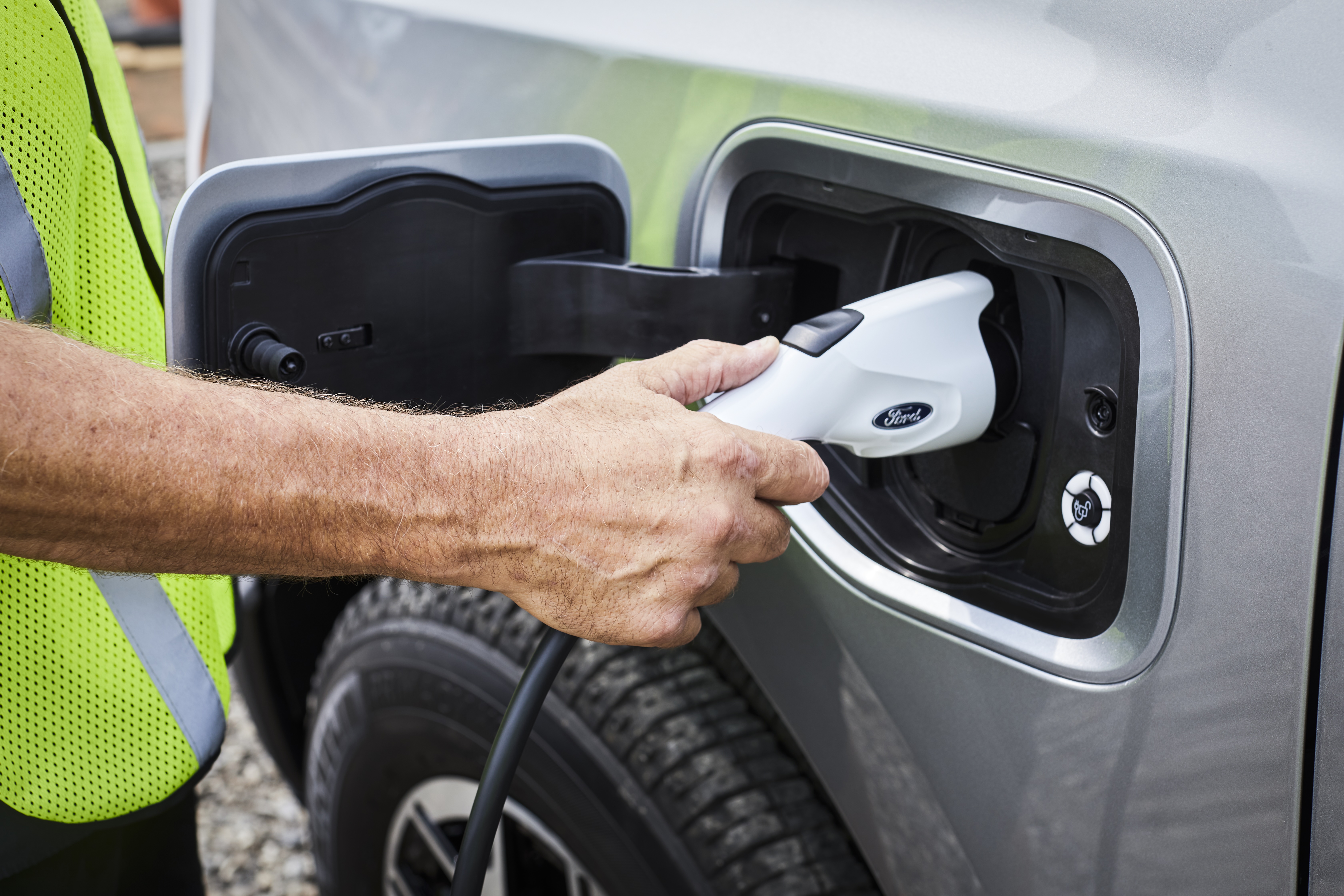 A man plugs a Ford Pro™ Charger into the charging port of an F-150® Lightning® truck.